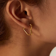 Close-up of a persons ear wearing the Eternal Love Earrings, featuring an abstract, irregular gold hoop. The persons hair is pulled back, revealing the elegant craftsmanship and minimalist design against their skin.
