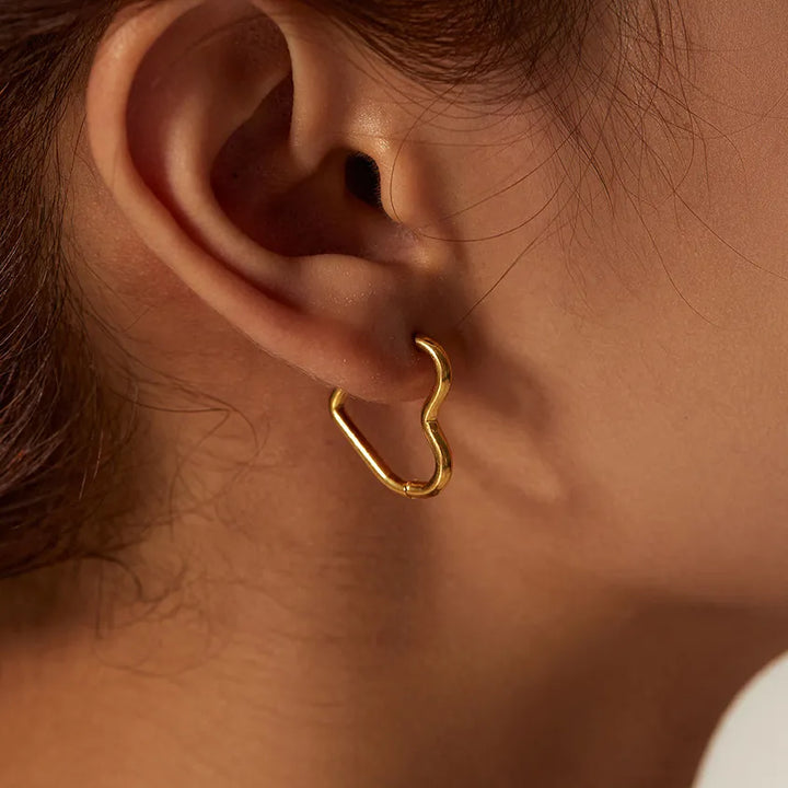 Close-up of a persons ear wearing the Eternal Love Earrings, featuring an abstract, irregular gold hoop. The persons hair is pulled back, revealing the elegant craftsmanship and minimalist design against their skin.