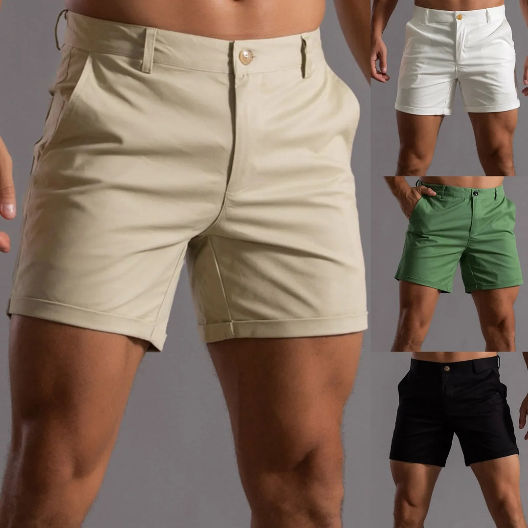 A man wearing beige shorts with a semi elastic waistband stands with hands by his sides. Smaller images to the right show the same tailored fit shorts in white, green, and black. The shorts have side pockets and a front button.