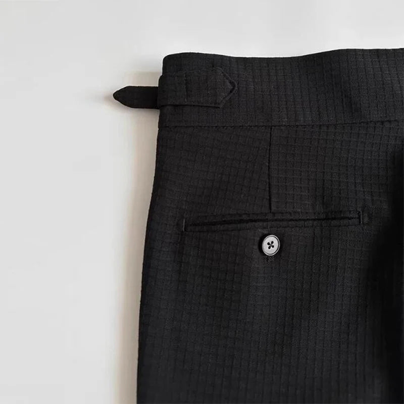 Close-up of the upper section of luxury tailored pants, featuring a back buttoned pocket, a belt loop with an extra tab, and a subtle grid pattern on the fabric.