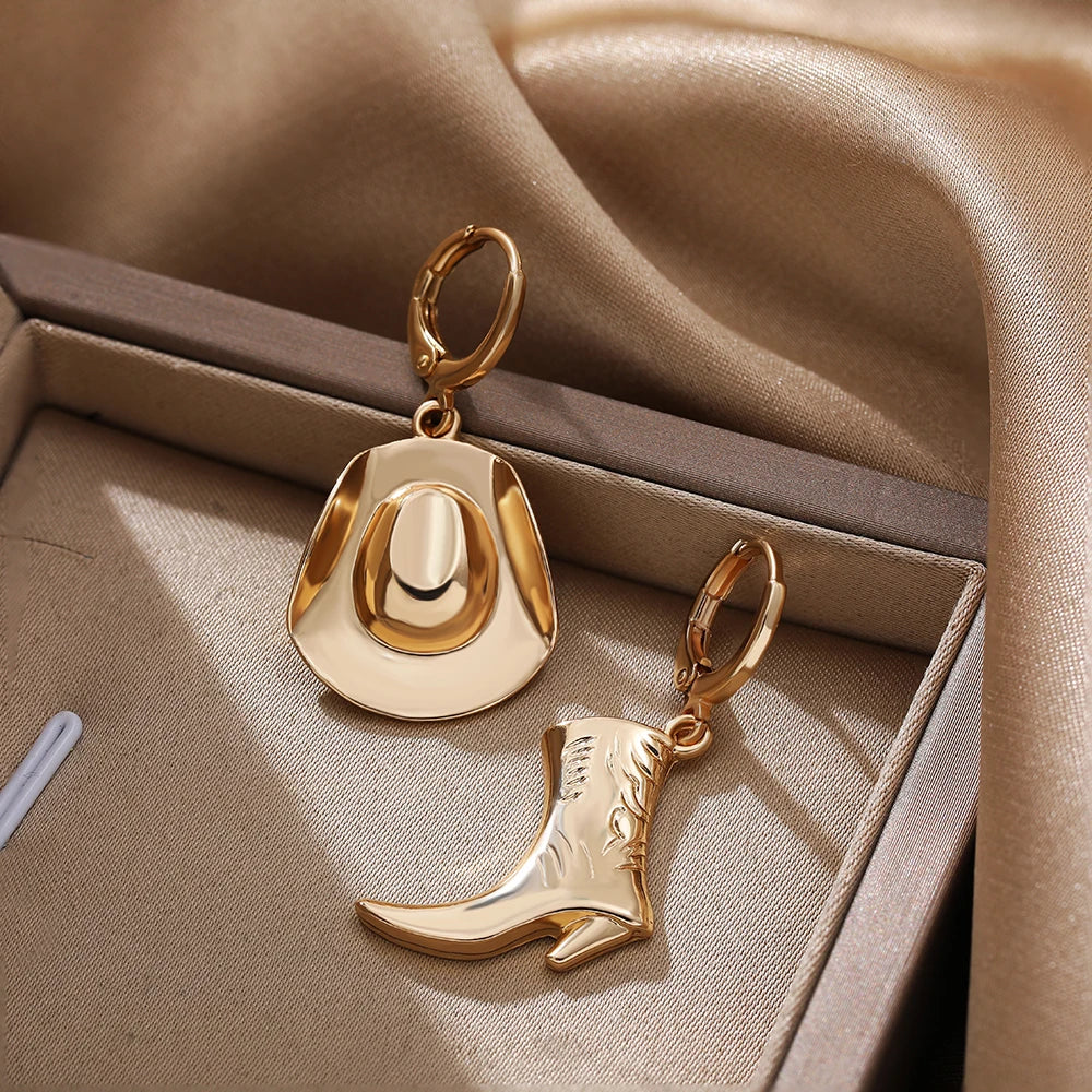 Gold cowboy hat earrings and a matching boot design rest in a beige jewelry box lined with satin fabric. The soft, elegant setting highlights these charming cowgirl accessories, perfect for lovers of western jewelry.