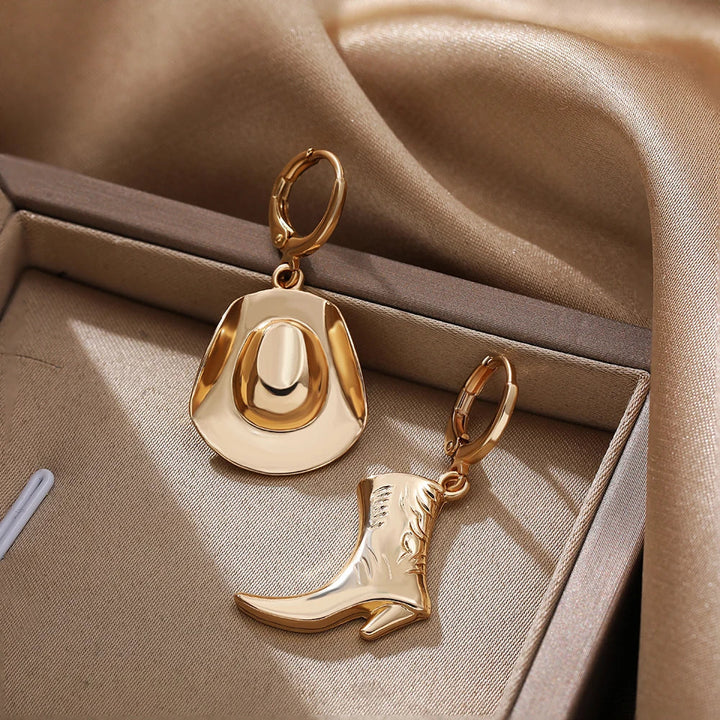 Gold cowboy hat earrings and a matching boot design rest in a beige jewelry box lined with satin fabric. The soft, elegant setting highlights these charming cowgirl accessories, perfect for lovers of western jewelry.