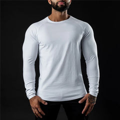 A man wearing a long sleeve fitted shirt stands against a black background, his hands resting by his sides. His head is slightly tilted down and his face is partially out of frame.