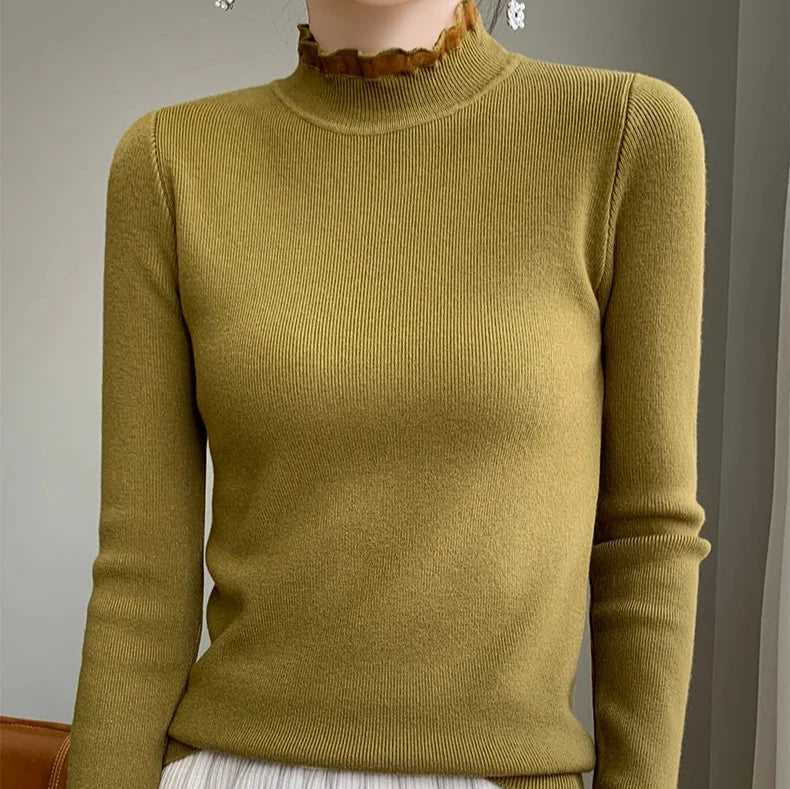 A person wearing a fitted, olive green ribbed sweater crafted from a cashmere blend with a high ruffled neckline and long sleeves, standing indoors against a neutral background.