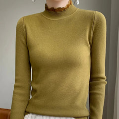 A person wearing a fitted, olive green ribbed sweater crafted from a cashmere blend with a high ruffled neckline and long sleeves, standing indoors against a neutral background.