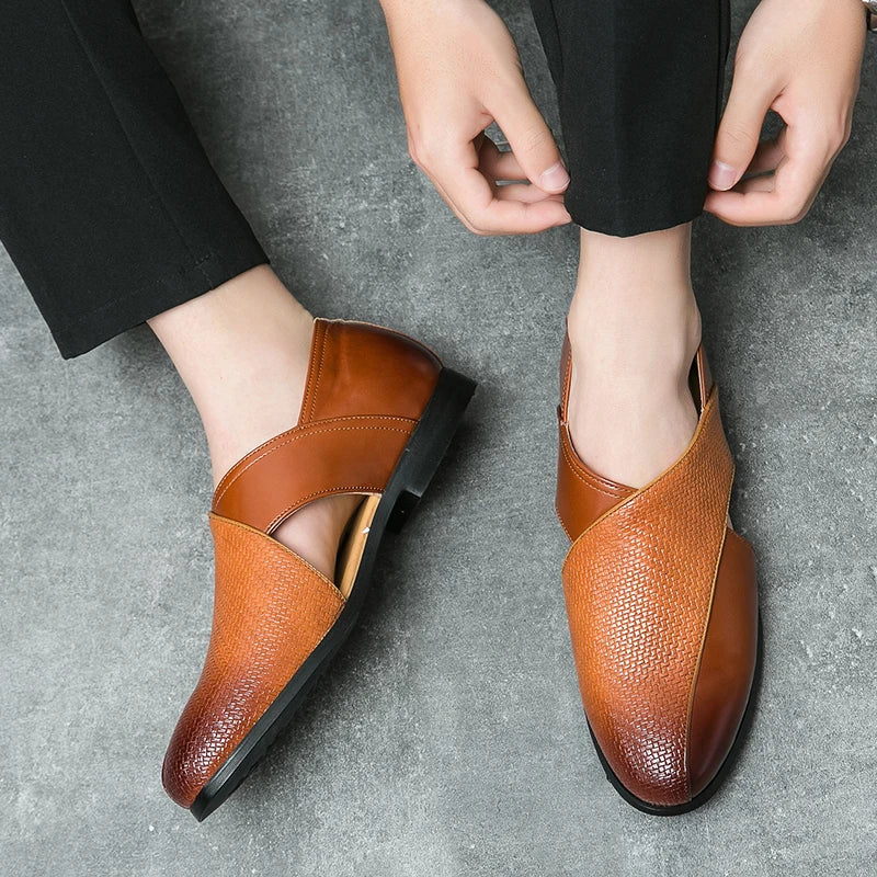 A person wearing black pants is putting on stylish genuine leather loafers with a textured pattern and durable outsole, sitting on a gray textured floor.