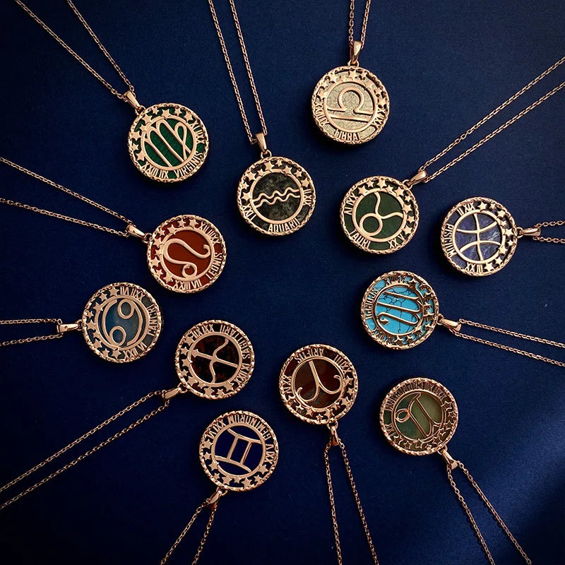 Twelve gold zodiac necklaces with round pendants, each featuring a different astrology symbol, are arranged in a circular pattern on a dark blue background.