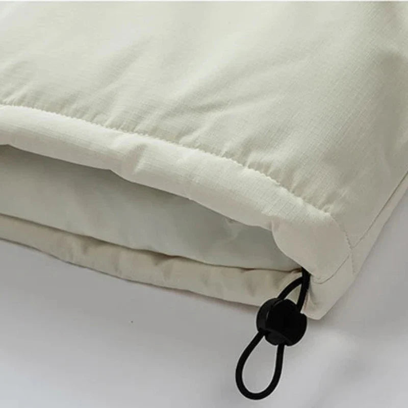 Close-up of a light beige windproof fabric jacket with an adjustable black drawstring and plastic toggle at the hem, showing the texture and stitching detail.