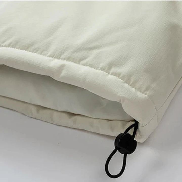 Close-up of a light beige windproof fabric jacket with an adjustable black drawstring and plastic toggle at the hem, showing the texture and stitching detail.