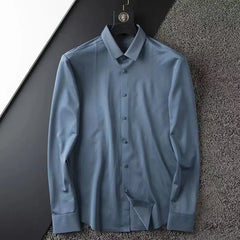 A business casual shirt, this light blue, long-sleeve dress shirt with subtle texture hangs on a black hanger against a textured grey surface. It features a classic collar and button-down front—perfect for spring.