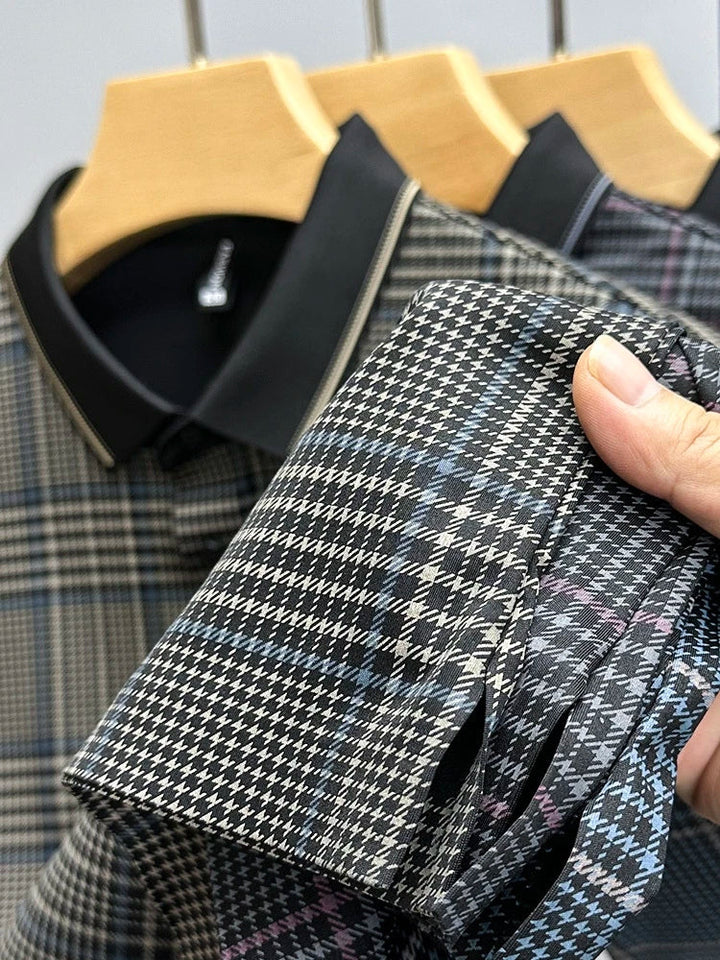 A hand holds the cuff of a plaid-patterned, breathable shirt, showcasing its detailed design. Two similar plaid shirts on wooden hangers are visible in the background.