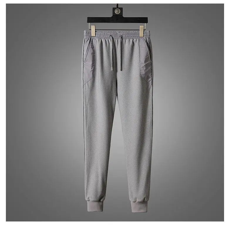 A pair of light gray jogger sweatpants with an elastic waistband, drawstring, side pockets, and cuffed ankles designed with moisture wicking fabric, hanging on a black hanger against a plain gray background.