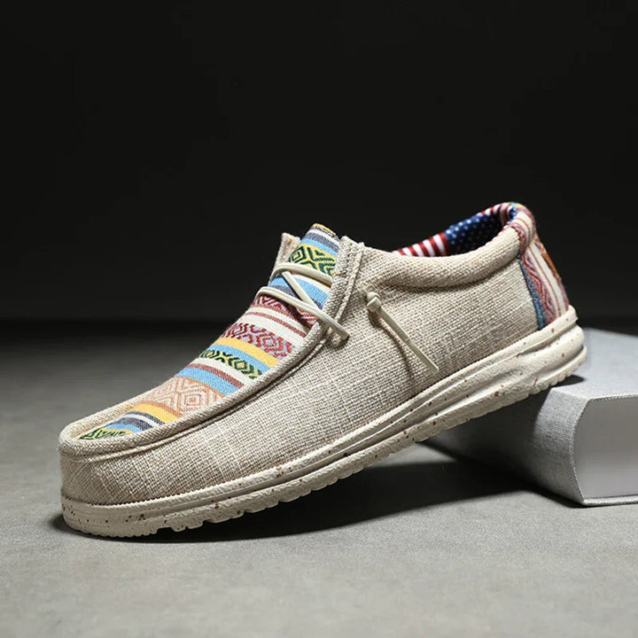 A casual beige shoe with a white sole and vibrant ethnic pattern on the woven upper, displayed at an angle against a neutral background.