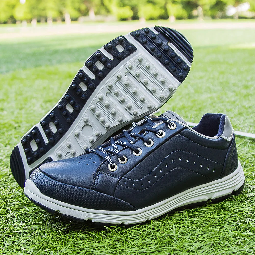 A pair of navy blue golf footwear with white soles displayed on green grass; one shoe is upright and the other is propped up to show the advanced cleat technology on its textured sole.