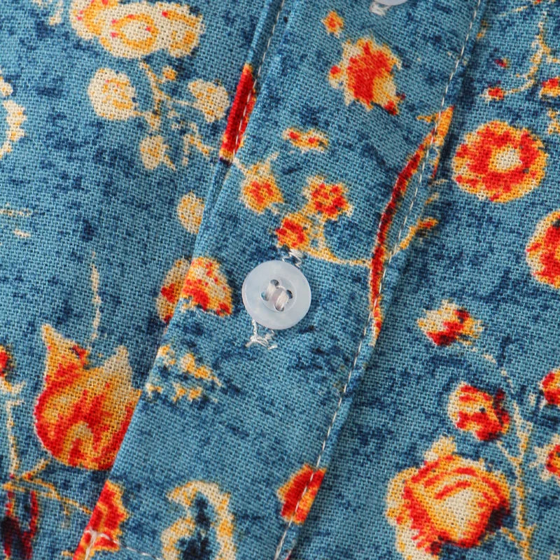 Close-up of a blue cotton shirt with an orange and yellow floral pattern, featuring a white button sewn on a stitched placket for a classic design.