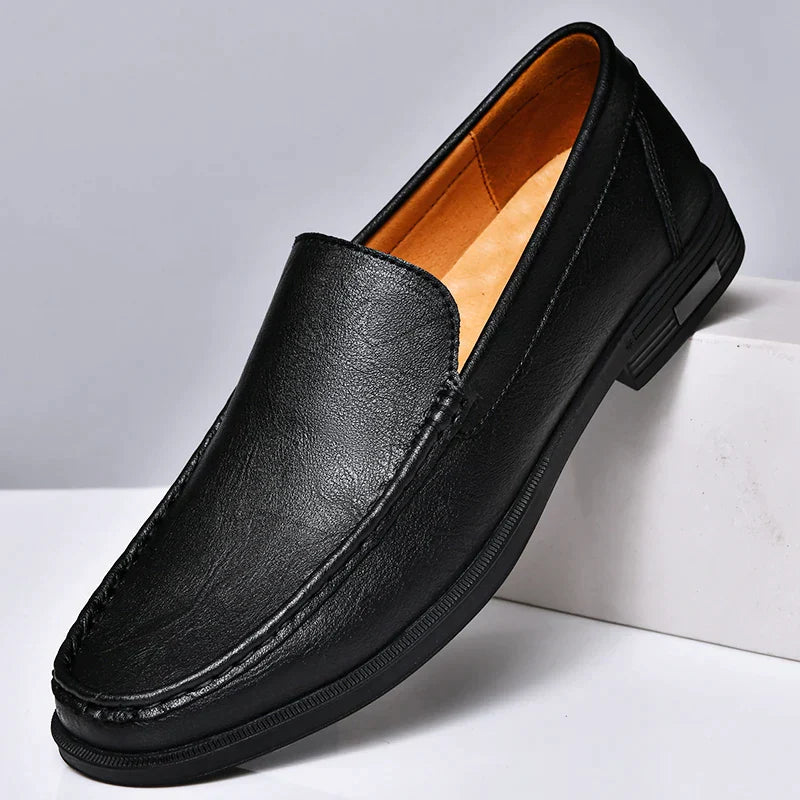 A black genuine leather loafer with a sleek design, visible stitching, and a tan interior, displayed at an angle on a white surface.