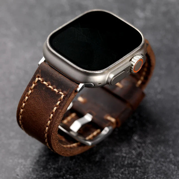 A modern smartwatch with a blank black screen and a brown Italian cowhide leather strap, featuring handcrafted saddle stitched white detailing, placed on a dark textured surface.
