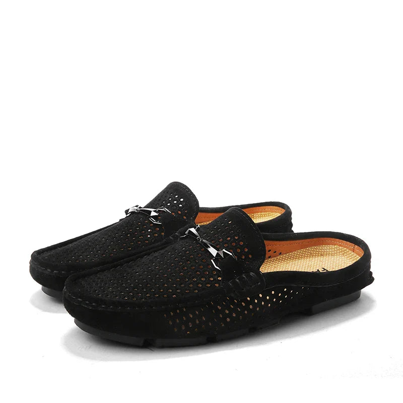 A pair of black slip-on breathable loafers with perforated uppers, open backs, and metal buckle details on the fronts. The shoes have tan insoles and black soles, making them perfect summer shoes.
