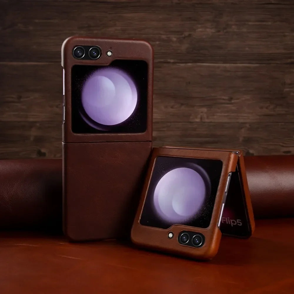 Two Samsung Galaxy Z Flip phones in genuine leather are shown, one upright and the other partially folded. Both display a purple orb on their front screens. The scene features a brown surface and a wooden backdrop, highlighting shockproof protection.