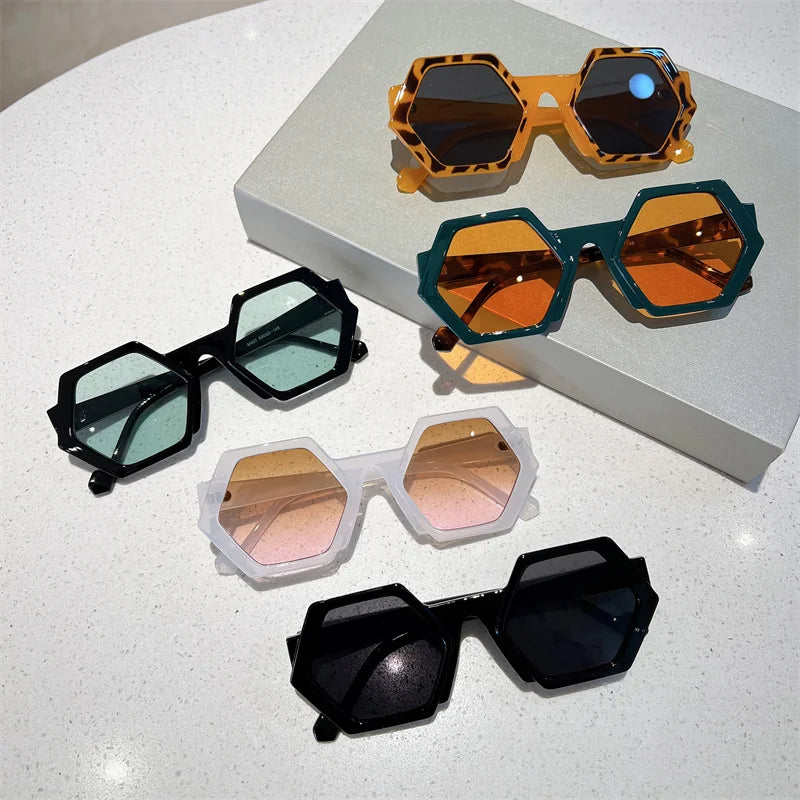 Five pairs of trend-forward, hexagonal frame sunglasses in various colors and lens tints are displayed on a white surface, with one pair resting on a box. Each offers UV400 protection for both style and eye safety.