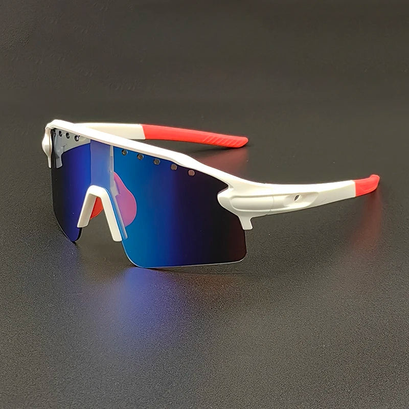 Sporty oversized sunglasses with white frames, red ear grips, and large blue-tinted, mirrored lenses are placed on a dark surface. These modern glasses feature an angular design and offer reliable UV400 protection.
