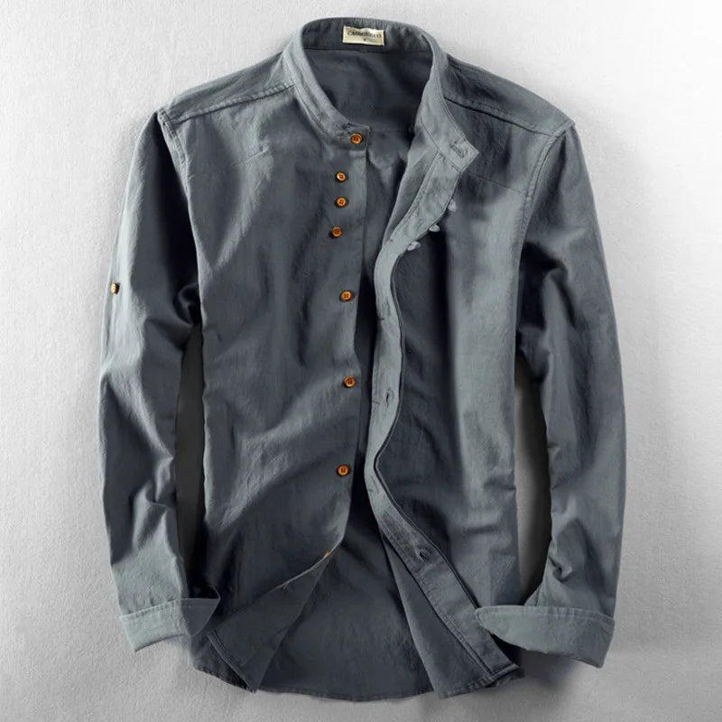 A long-sleeve, button-up grey Japanese inspired overshirt featuring brown buttons, a mandarin collar, and a relaxed fit, crafted from 100% cotton and laid flat on a light grey surface.