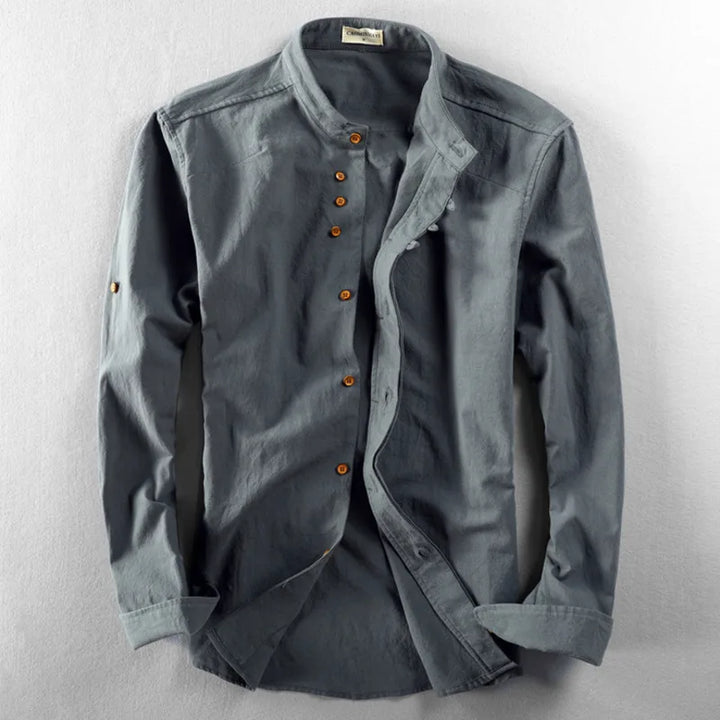 A long-sleeve, button-up grey Japanese inspired overshirt featuring brown buttons, a mandarin collar, and a relaxed fit, crafted from 100% cotton and laid flat on a light grey surface.