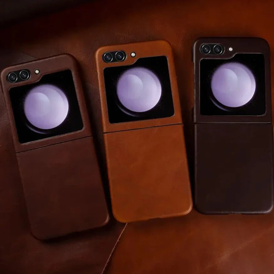 Three genuine leather phone cases with built-in lens protectors offer shockproof protection for your Samsung Galaxy Z Flip. Displayed side by side on a brown leather surface, each case features a raised circular lens cover above the camera area.