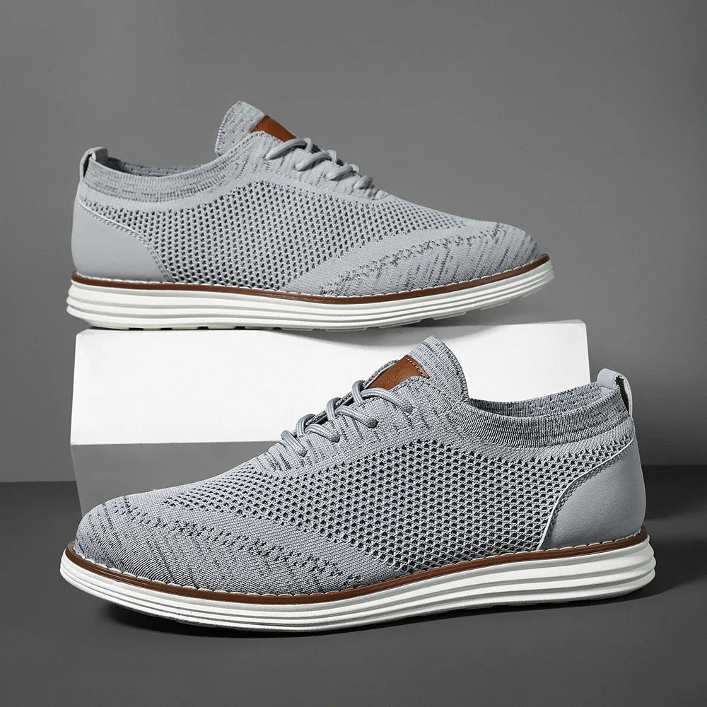 A pair of light gray, breathable knit sneakers with white soles, subtle brown accents on the tongue, and white laces, displayed against a gray background with one shoe elevated on a white block for effortless casual style.