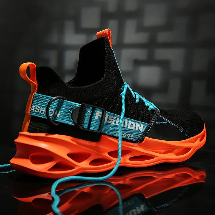 A stylish black Extreme VS7 Sneaker with a bright orange sole and accents, blue laces, and a blue strap labeled FASHION. This streetwear sneaker is displayed against a dark, blurred background.