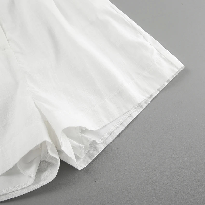 A close-up of the lower portion of a pair of white shorts made from a lightweight fabric, perfect for summer outings, displayed on a flat gray surface.