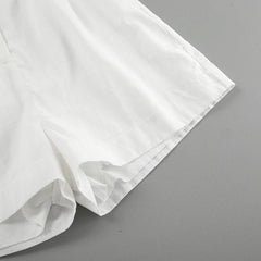 A close-up of the lower portion of a pair of white shorts made from a lightweight fabric, perfect for summer outings, displayed on a flat gray surface.