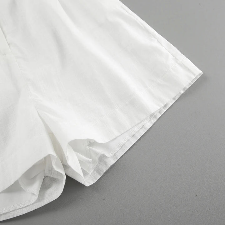 A close-up of the lower portion of a pair of white shorts made from a lightweight fabric, perfect for summer outings, displayed on a flat gray surface.