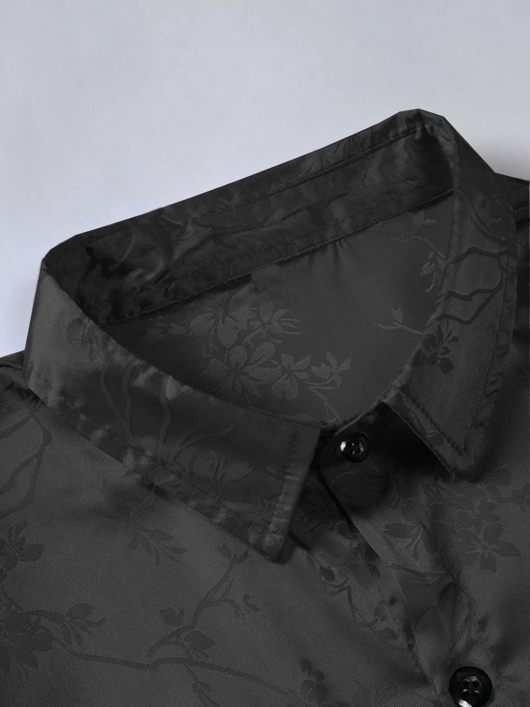 Close-up of a black collared shirt with a subtle floral pattern and black buttons, crafted from breathable fabric—perfect for men's summer shirts, displayed against a light background.