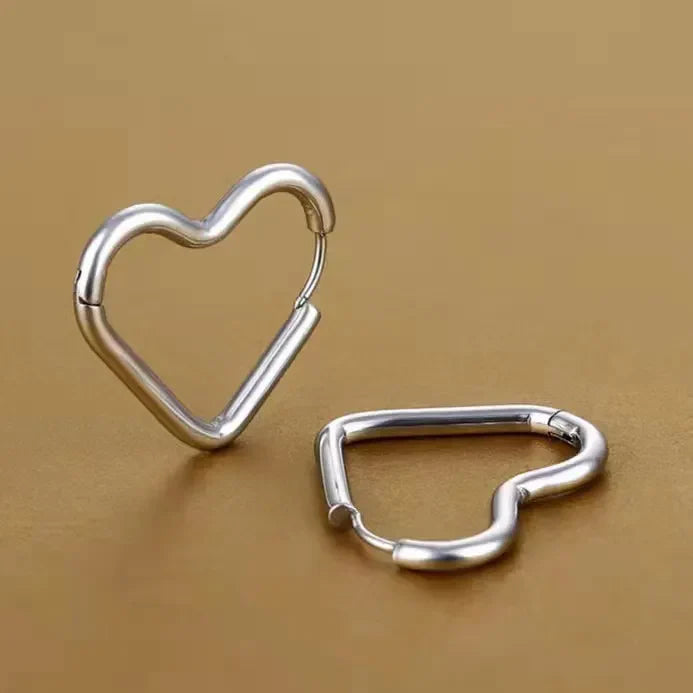 Two metallic heart-shaped Eternal Love Earrings rest on a smooth, gold-colored surface. One stands upright while the other lies flat, both highlighting their minimalist design and elegant craftsmanship.
