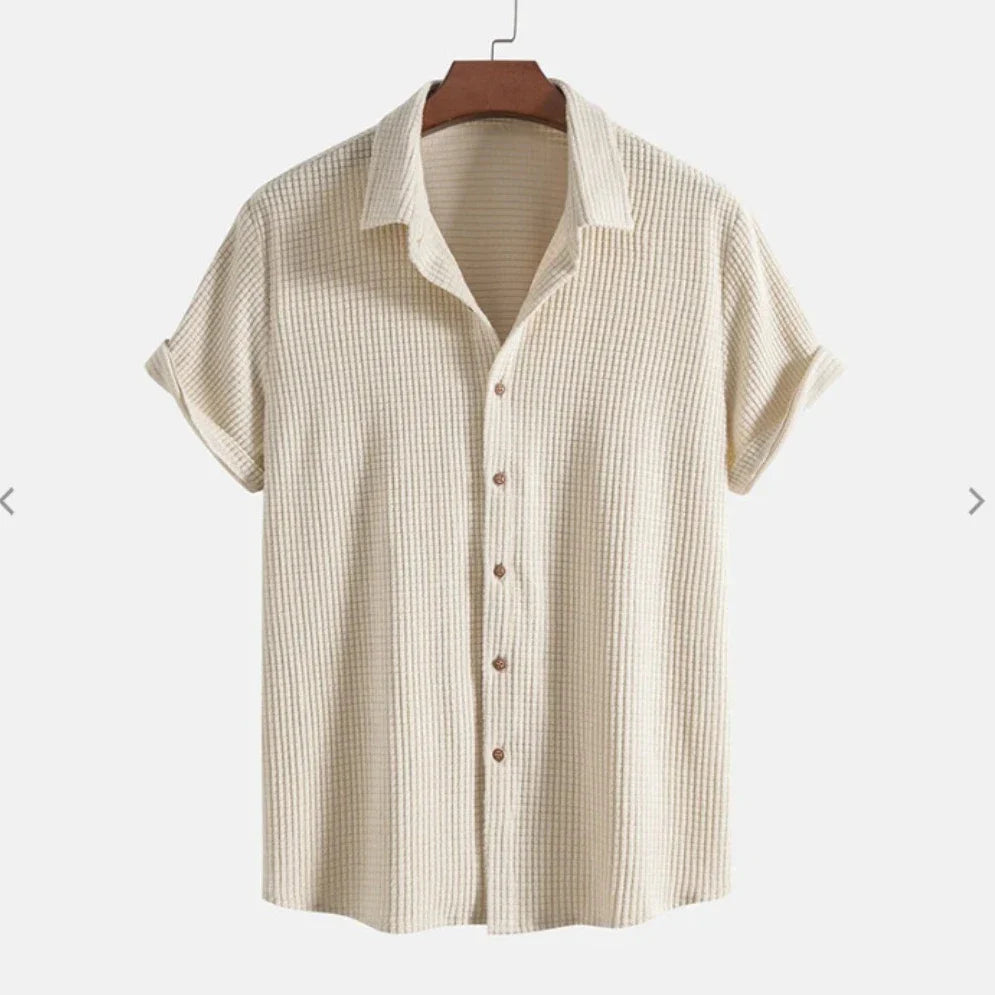 A short-sleeve, cream-colored Bayside Shirt featuring a textured button-up design and collar, crafted from a breathable cotton blend, displayed on a wooden hanger against a plain background.