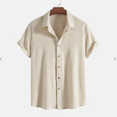 A short-sleeve, cream-colored Bayside Shirt featuring a textured button-up design and collar, crafted from a breathable cotton blend, displayed on a wooden hanger against a plain background.