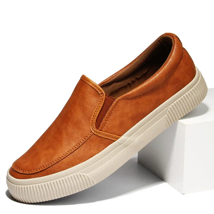 A brown men’s slip-on casual shoe with a hybrid rubber sole and leather insole, displayed on a white block against a plain background.