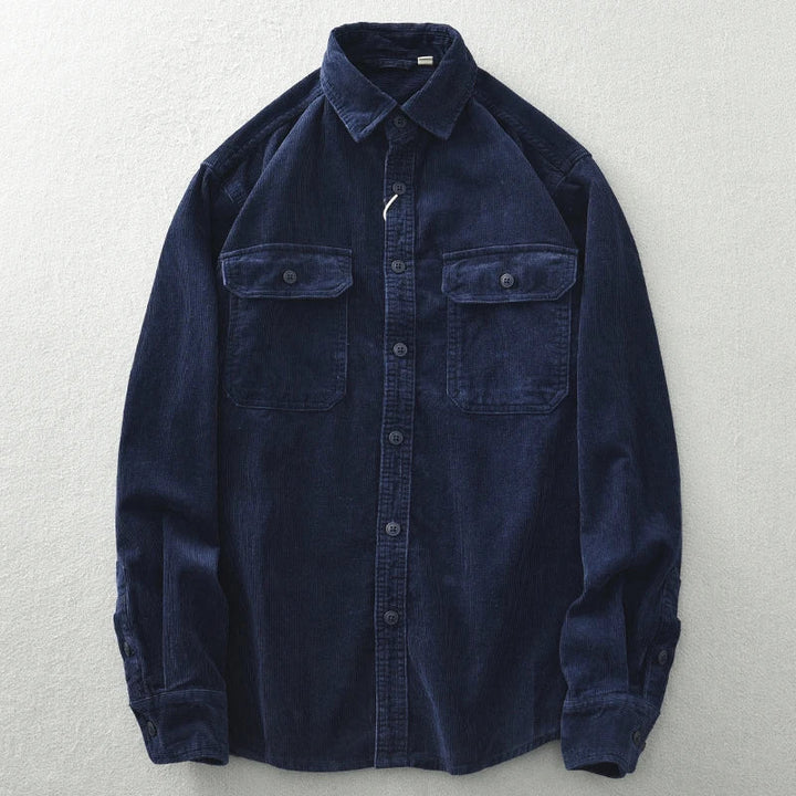A long-sleeve, dark blue button-up shirt crafted from heavyweight cotton corduroy, featuring a button-down front, two chest pockets with flaps, and buttoned cuffs, laid flat on a light-colored surface.