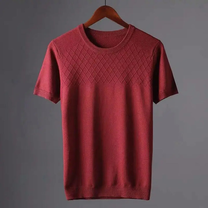 A classic fit maroon knit sweater with a round neckline and diamond-patterned stitching across the chest, hanging on a wooden hanger against a plain gray background.