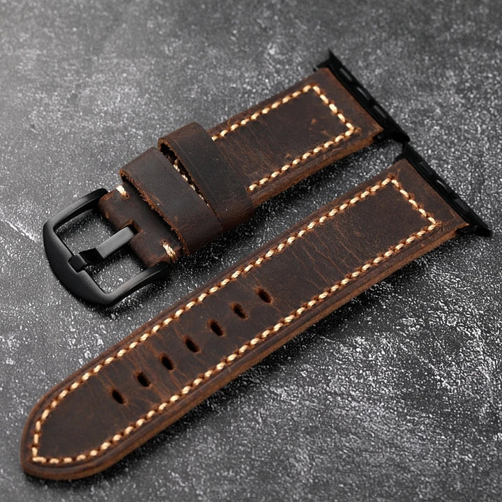 A brown Italian cowhide leather watch strap with visible beige saddle stitching and a black metal buckle, displayed on a textured dark background. The handcrafted strap is shown in two separate pieces.