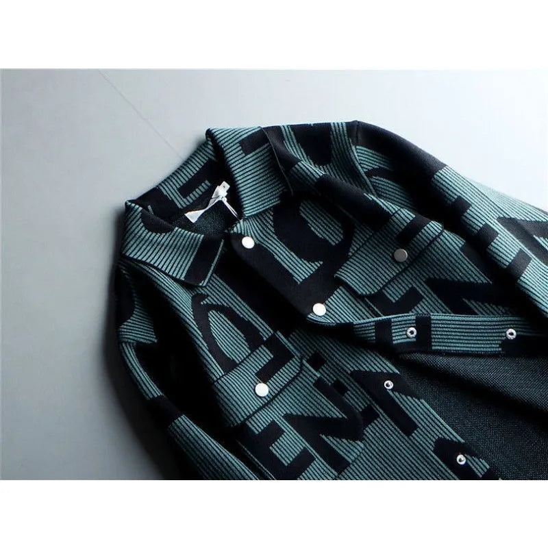 A close-up of a mens long sleeve coat with a bold, black and teal graphic pattern featuring large, overlapping letters. This Korean loose fit jacket is laid flat on a light gray surface.