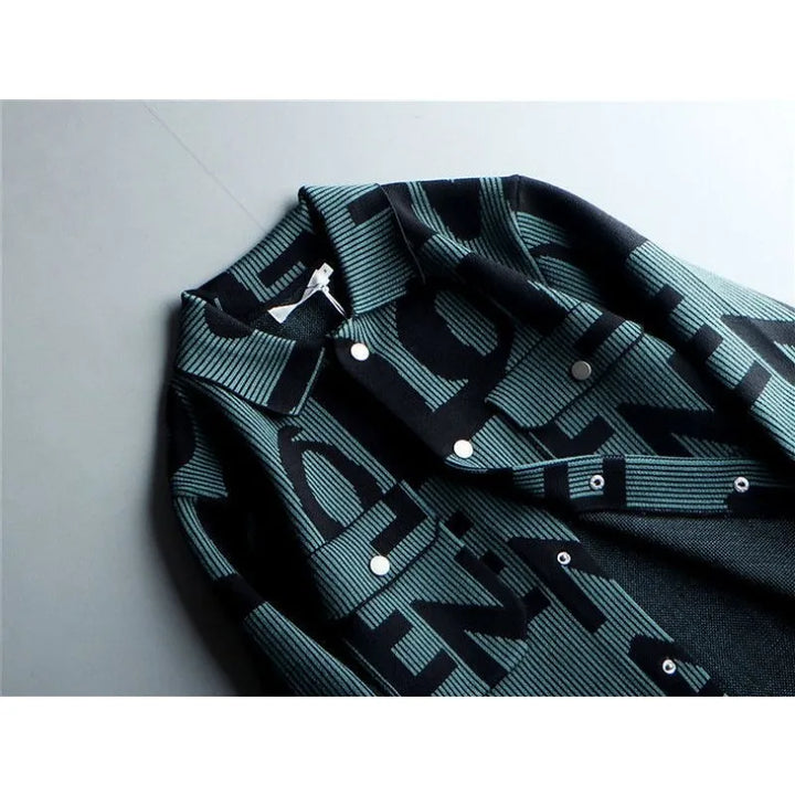 A close-up of a mens long sleeve coat with a bold, black and teal graphic pattern featuring large, overlapping letters. This Korean loose fit jacket is laid flat on a light gray surface.