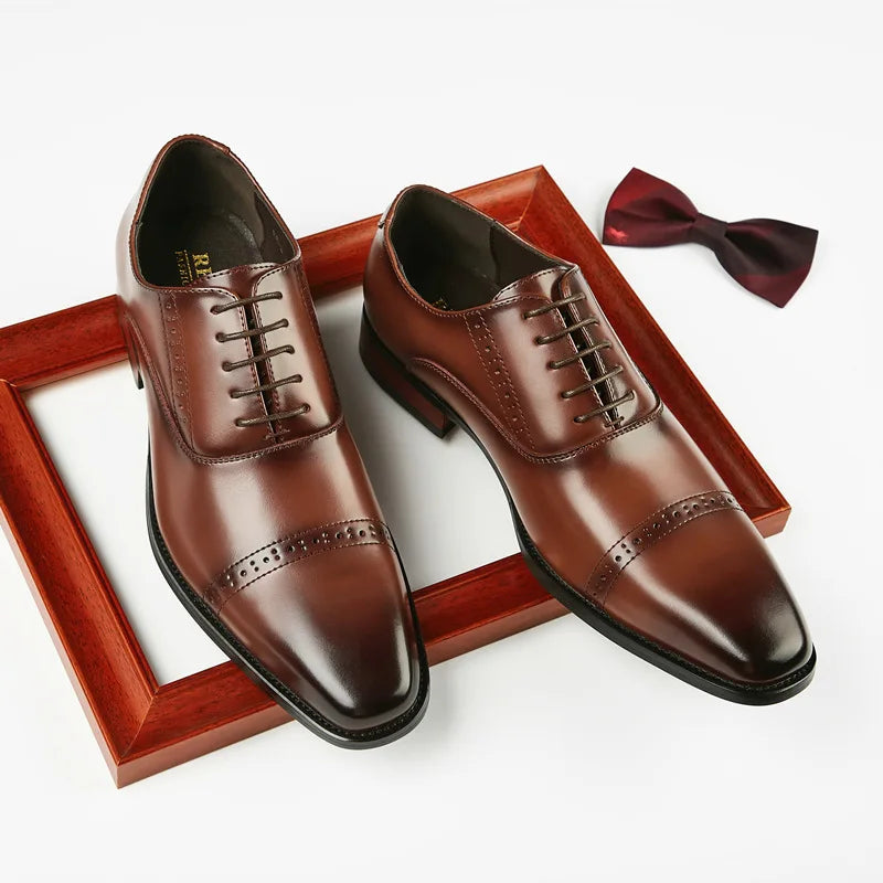A pair of polished brown Italian leather dress shoes with laces and hand-stitched detailing rest on a wooden picture frame, next to a dark red bow tie on a white background.