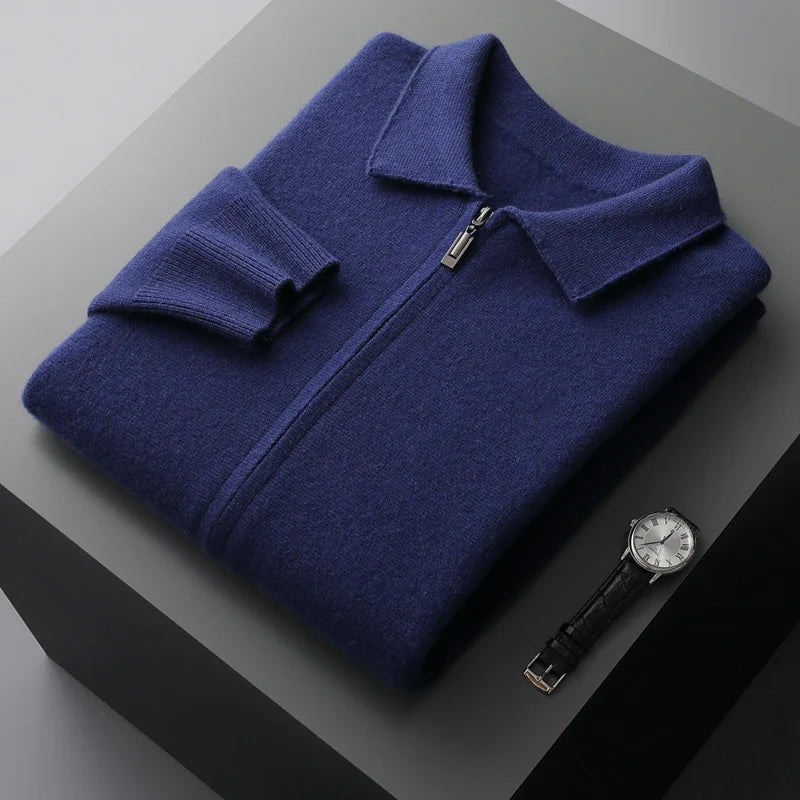 A neatly folded navy blue merino wool zip-up sweater with a collar is placed on a gray surface next to a black leather strap wristwatch with a silver face, offering natural temperature regulation and style.