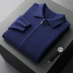 A neatly folded navy blue merino wool zip-up sweater with a collar is placed on a gray surface next to a black leather strap wristwatch with a silver face, offering natural temperature regulation and style.