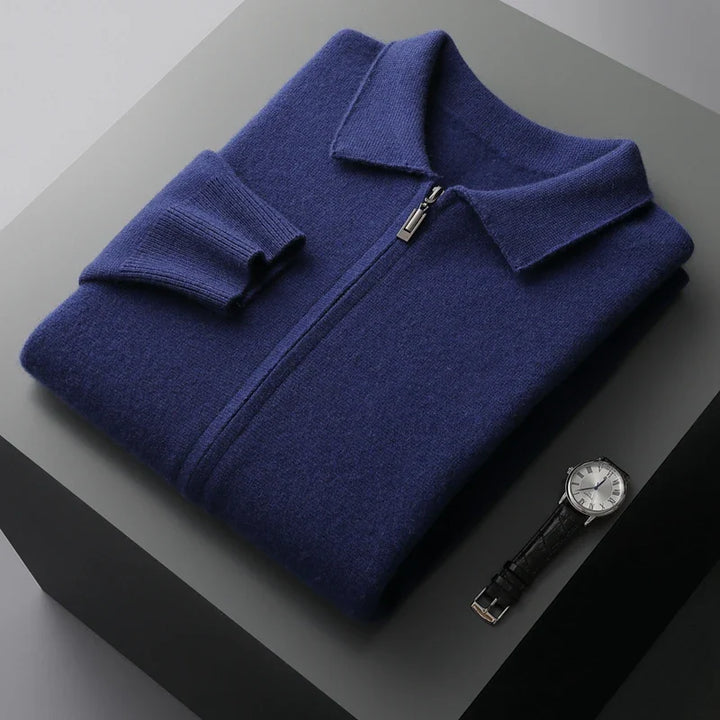 A neatly folded navy blue merino wool zip-up sweater with a collar is placed on a gray surface next to a black leather strap wristwatch with a silver face, offering natural temperature regulation and style.