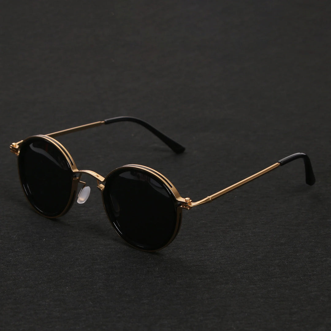Round black Ruby Ray Sunglasses with thin gold metal frames and black temple tips, featuring UV400 protection, displayed on a dark textured surface.