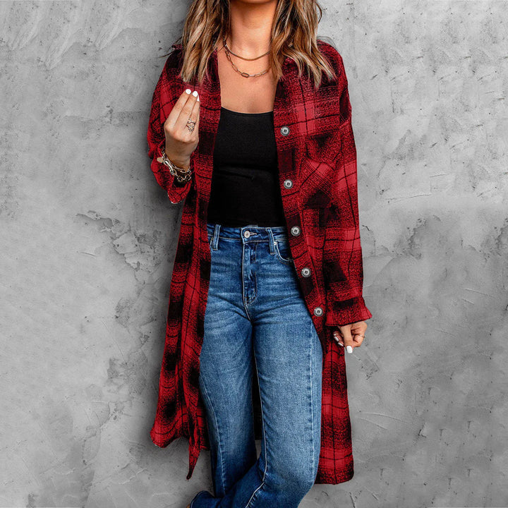 A woman stands against a gray textured wall wearing a long red and black plaid button-down shirt over a black top and blue jeans. Her hand is raised near her face, showing effortless layering with this lightweight flannel. Her hair is loose and wavy.