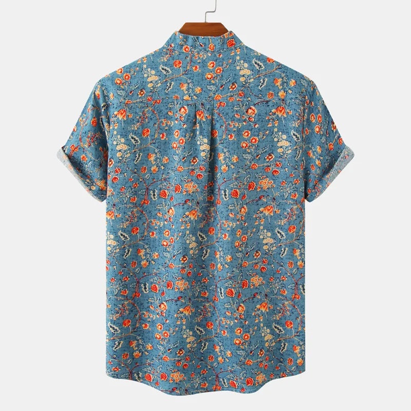A classic design, this short-sleeve button-up cotton shirt showcases a blue background with a colorful floral pattern in red, orange, yellow, and white, displayed on a hanger against a plain background.